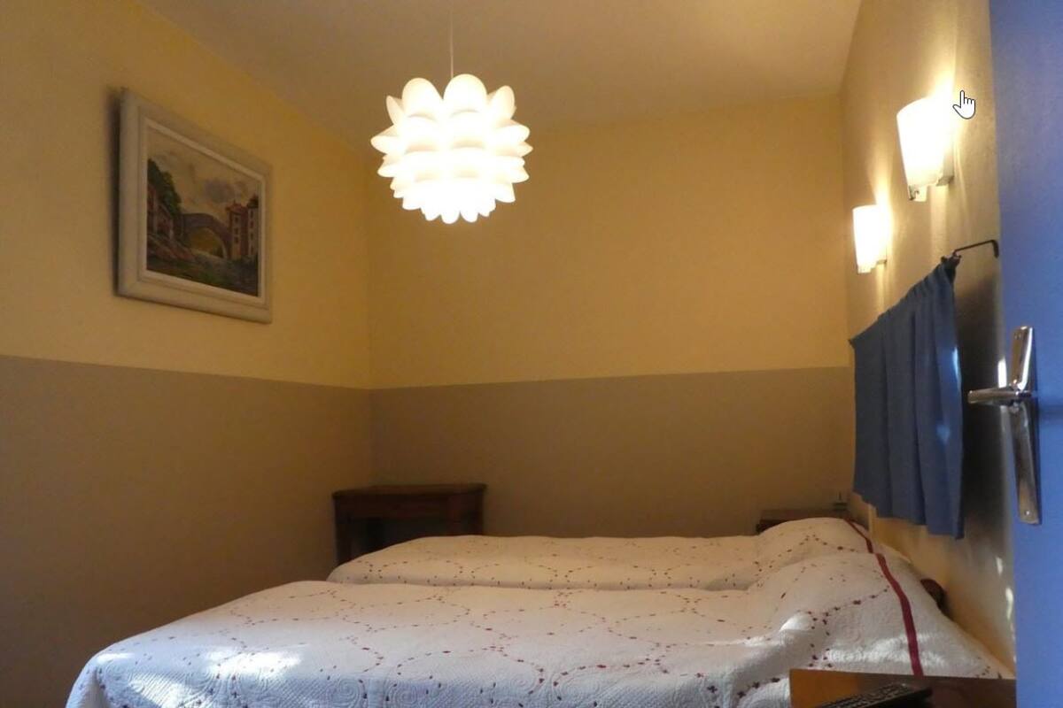 Ein Hotelzimmer mit Bett, einer Pendelleuchte, einem Bild an der Wand und einer Tür mit Handtuchhalter.