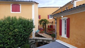 Un carrer estret amb edificis grocs, persianes vermelles i un petit pont.