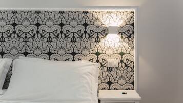 A neatly made bed with white linens, a bedside table with a lamp, and a wall with a black and white floral pattern.