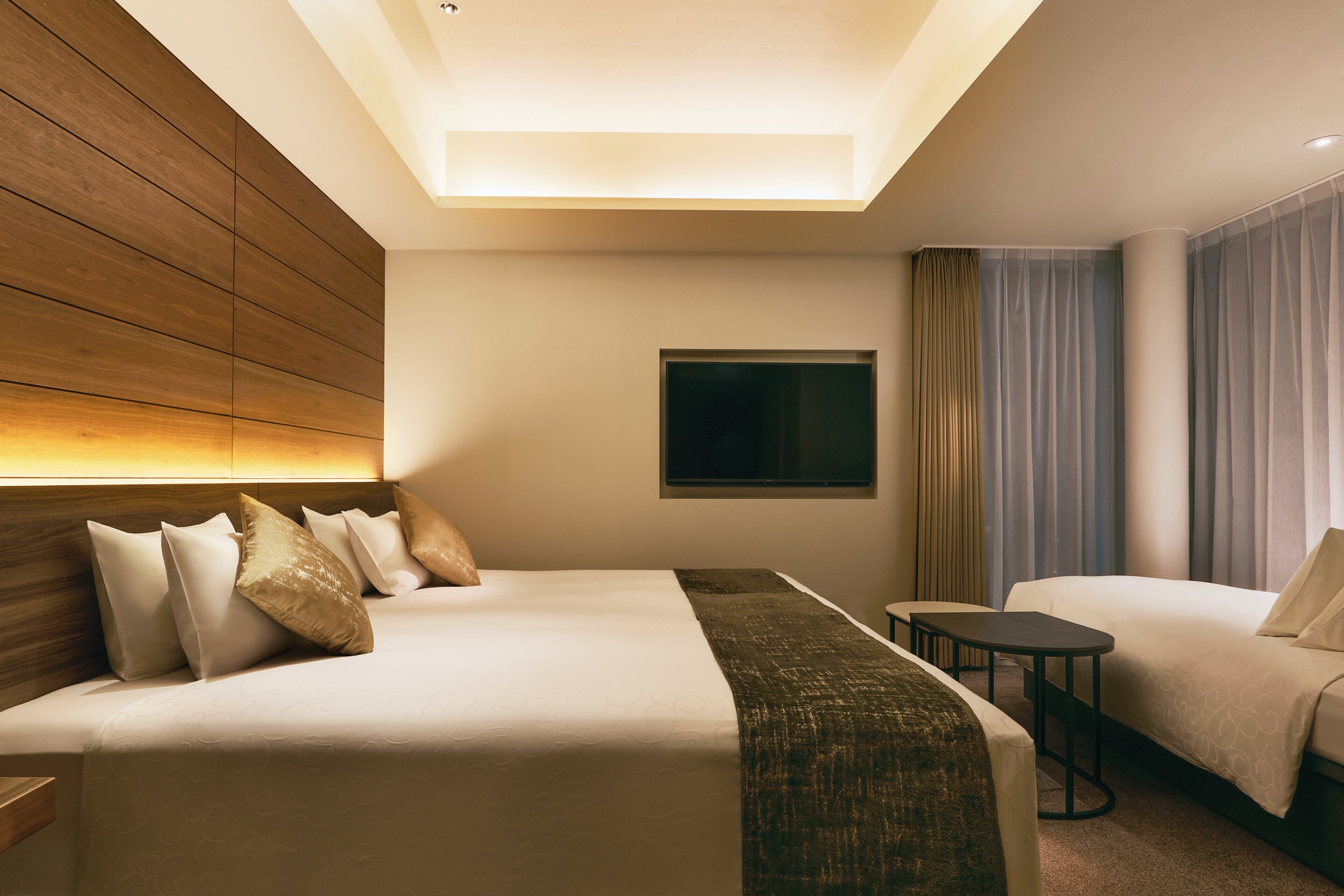 A hotel room with a large bed, a smaller bed, a desk, and a TV on the wall.