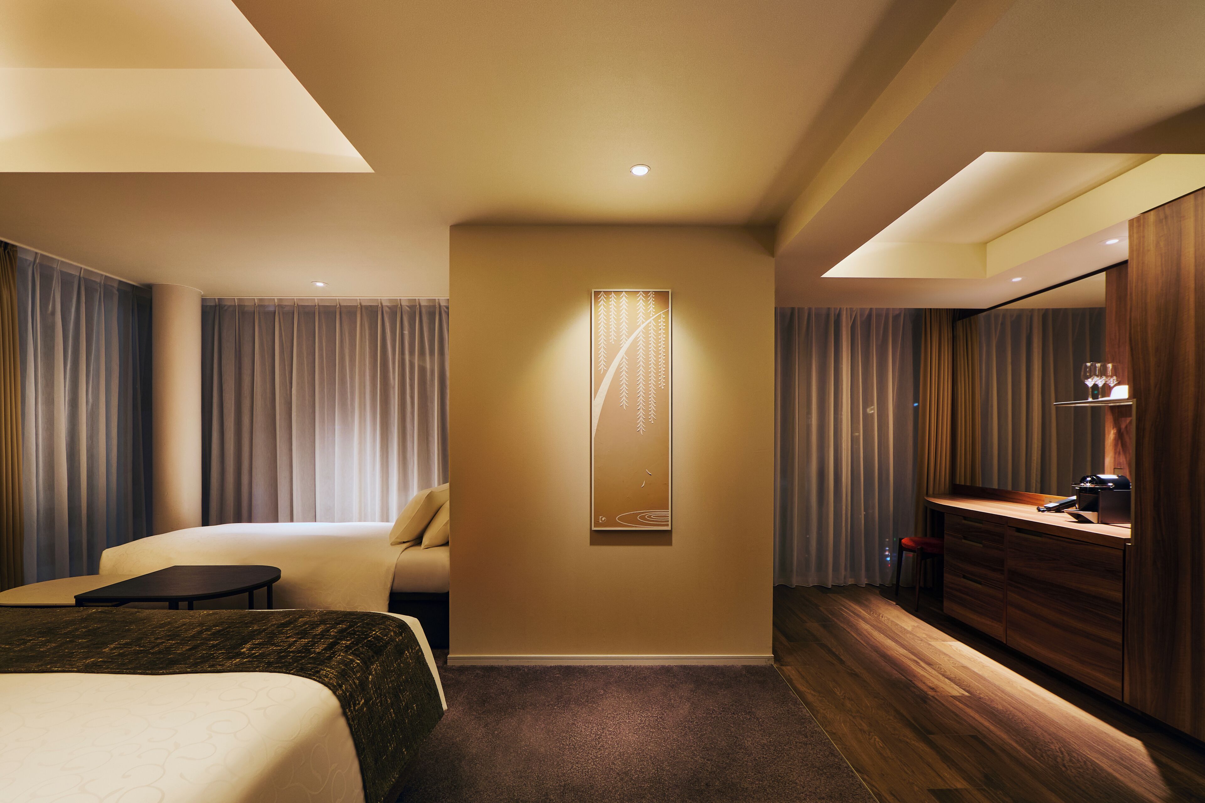 A hotel room with a bed, a desk, a chair, a mirror, and a wall-mounted artwork.
