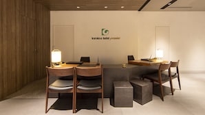 A modern reception area with a wooden reception desk, two chairs, a small table, and a logo on the wall. - karaksa hotel premier Tokyo Ginza (Tokyo)