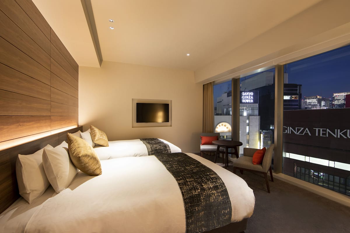 Hotellihuone, jossa on kaksi sänkyä, televisio, tuoli ja näkymä kaupungin siluettiin.
