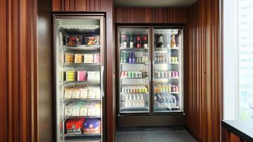 A corner with two glass-fronted beverage dispensers stocked with various drinks and snacks.