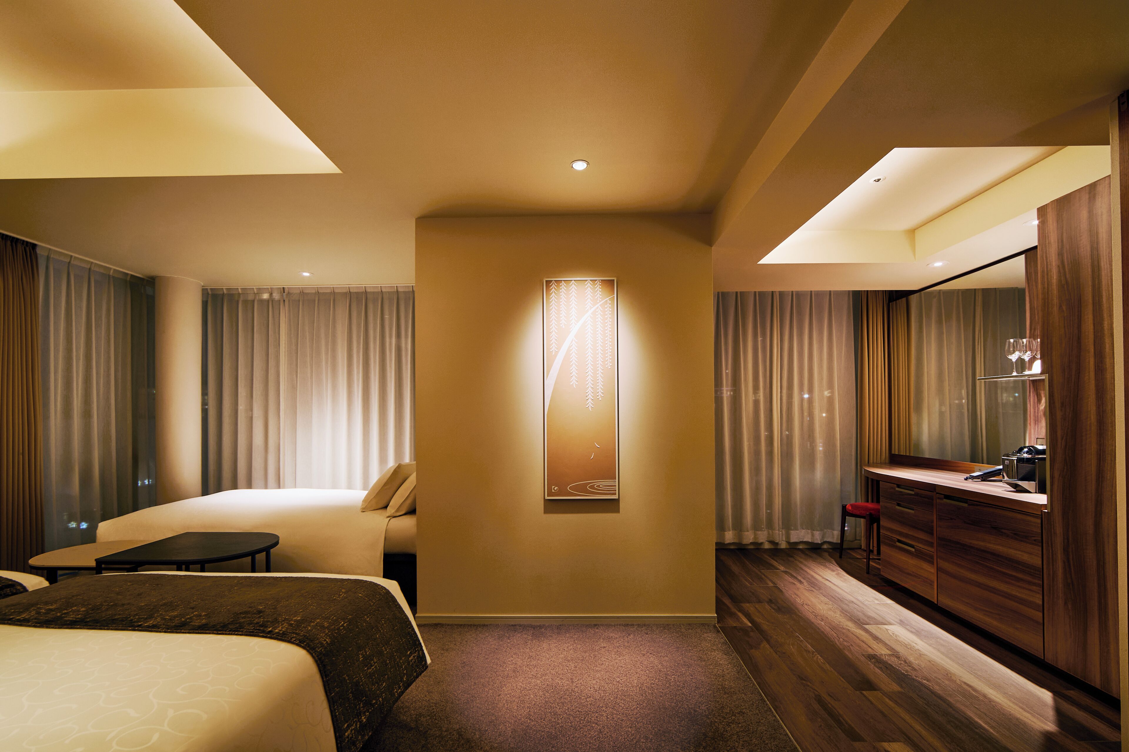 A hotel room with a bed, a desk, a chair, a mirror, and a wall-mounted artwork.