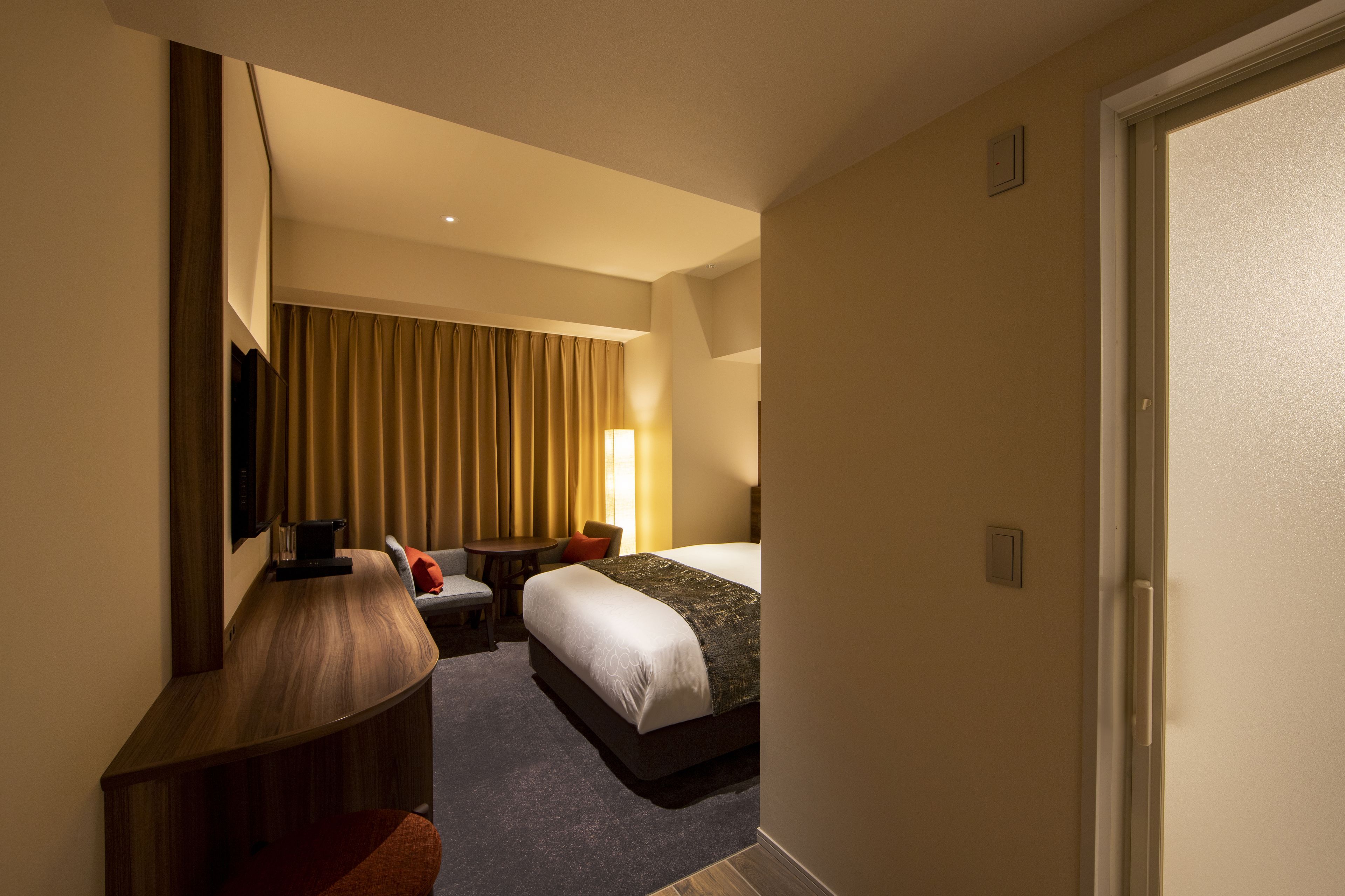 A hotel room with a bed, a desk, a chair, and a small table.