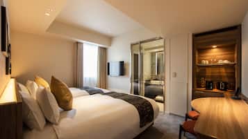 A modern hotel room with a large bed, a dining area, and a glass door leading to a bathroom.