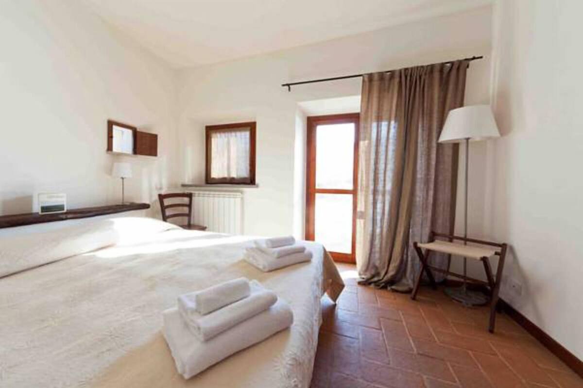 Habitación de hotel con una cama grande, un escritorio, una silla, una lámpara y vistas al exterior.