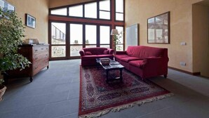 A spacious living room with a red sofa, a coffee table, and a large window offering a view of the outdoors. - La Perticara (Acquasparta)