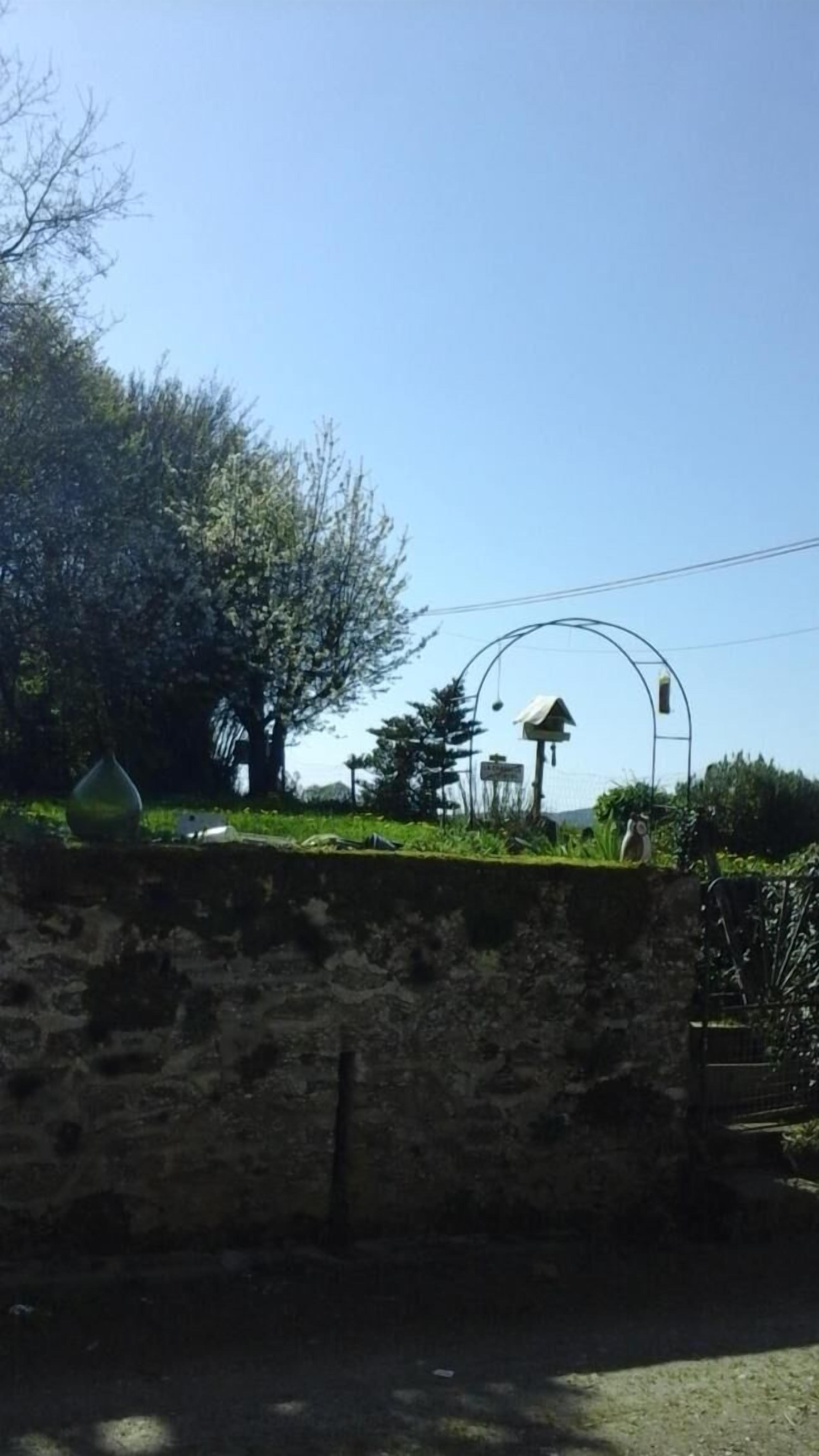 Eine Steinsäule, ein Metallbogen und ein Baum in sonniger Umgebung.