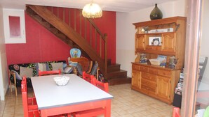 Een eethoek met een rode tafel en stoelen, een houten trap en een kast met diverse spullen.