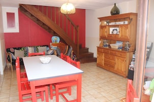 Un comedor con mesa y sillas rojas, una escalera de madera y un armario con diversos objetos.