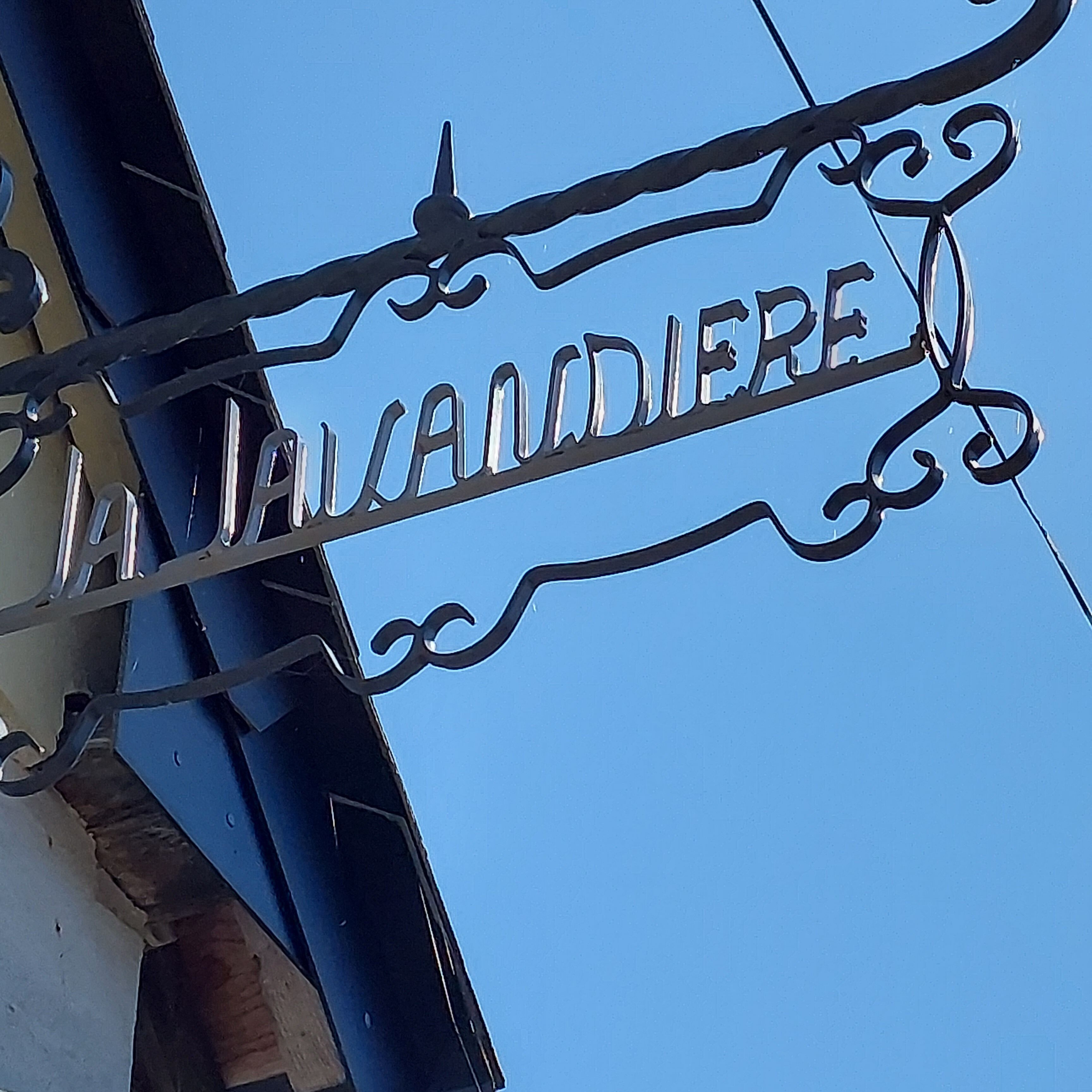 Une plaque métallique portant l’inscription « LA CALANDIERIA », sur fond de ciel bleu clair.