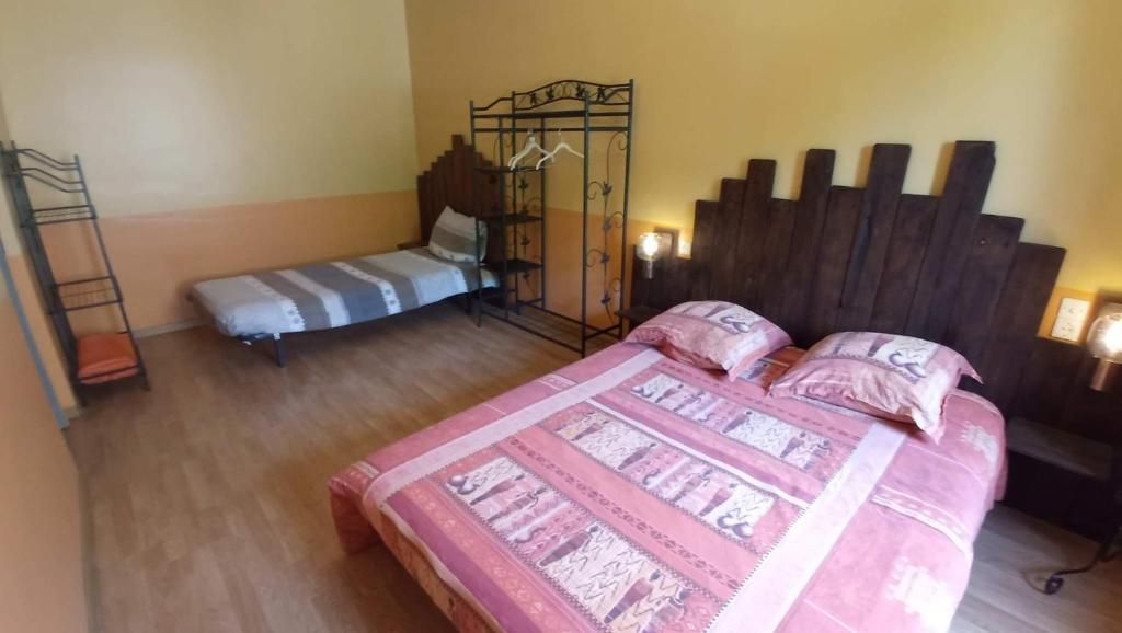 A bedroom with a large bed, a smaller bed, a metal wardrobe, and a bedside table with a lamp.