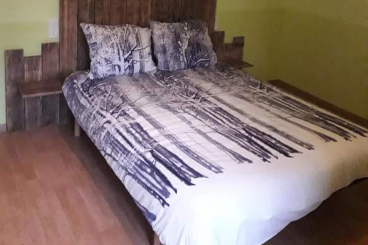 A bedroom with a wooden headboard, a patterned bedspread, and a green wall.