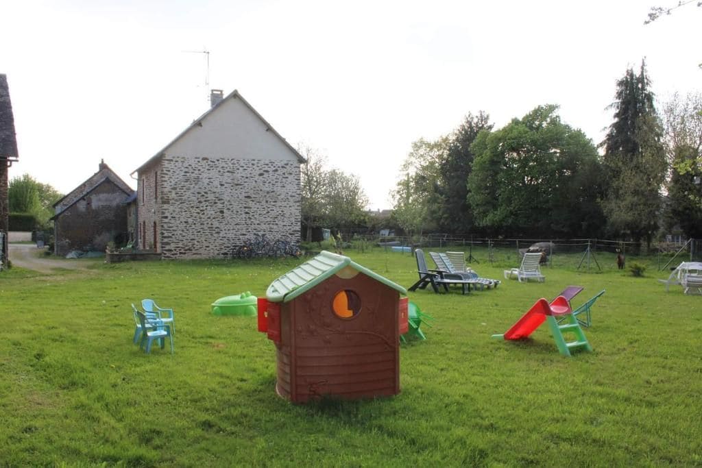 A grassy outdoor area with a wooden playhouse, a stone building, and outdoor furniture.