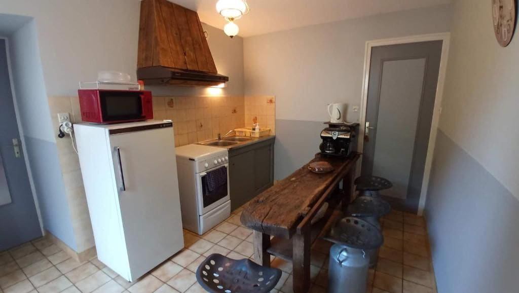 Une cuisine compacte équipée d’un réfrigérateur, d’un four à micro-ondes, d’une cuisinière et d’une table en bois avec des tabourets.