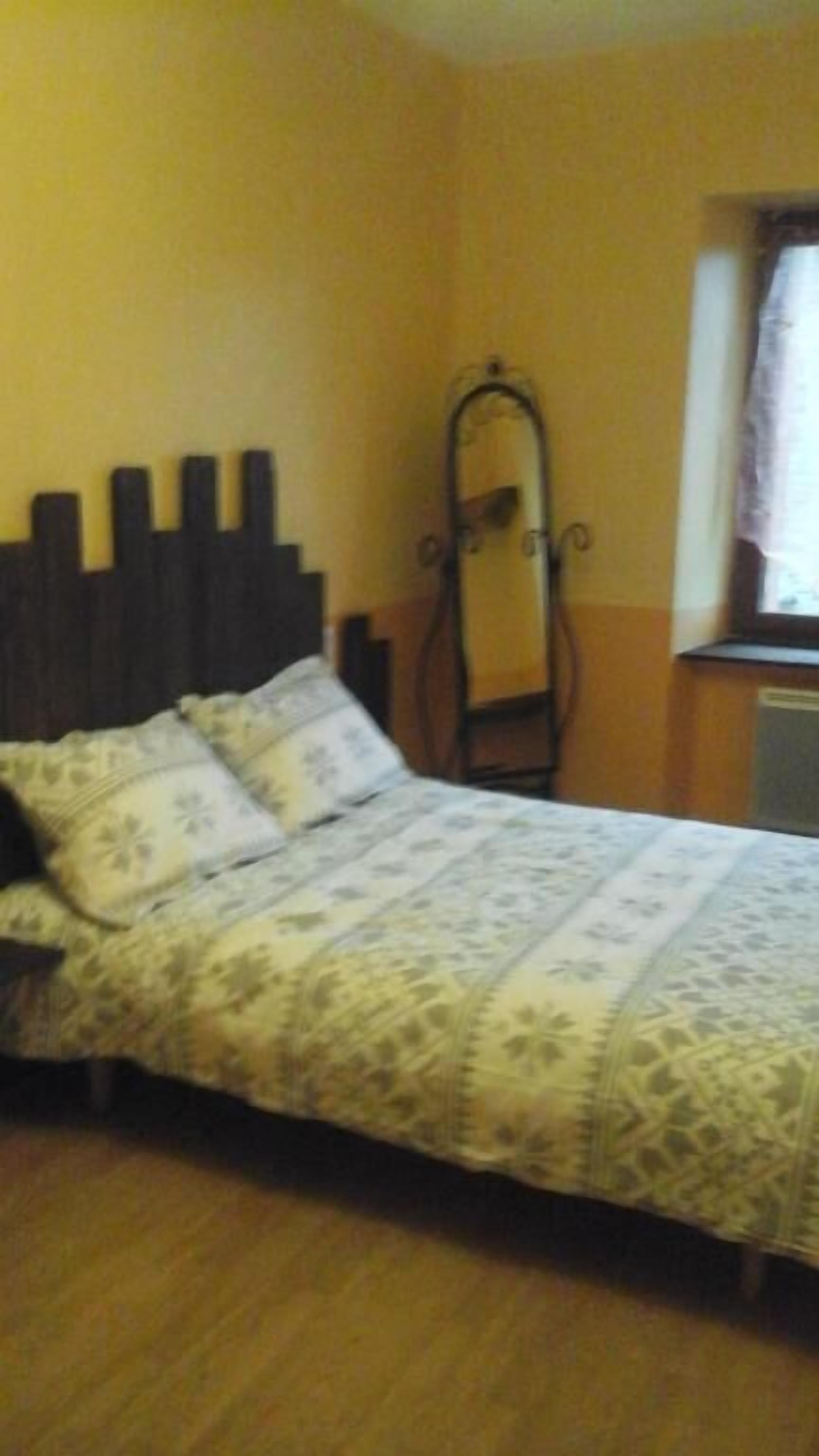 A bed with a patterned bedspread, a wooden headboard, and a mirror on the wall.