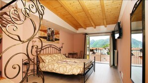 Une chambre à coucher avec un lit, un plafond en bois, un balcon donnant sur les montagnes et un tableau accroché au mur.