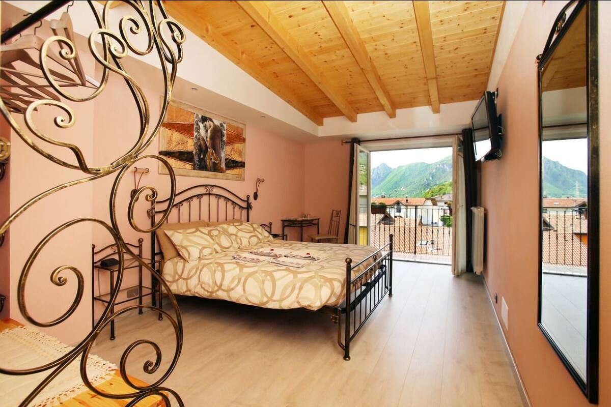 Un dormitorio con cama, techo de madera, balcón con vista a montañas y un cuadro en la pared.