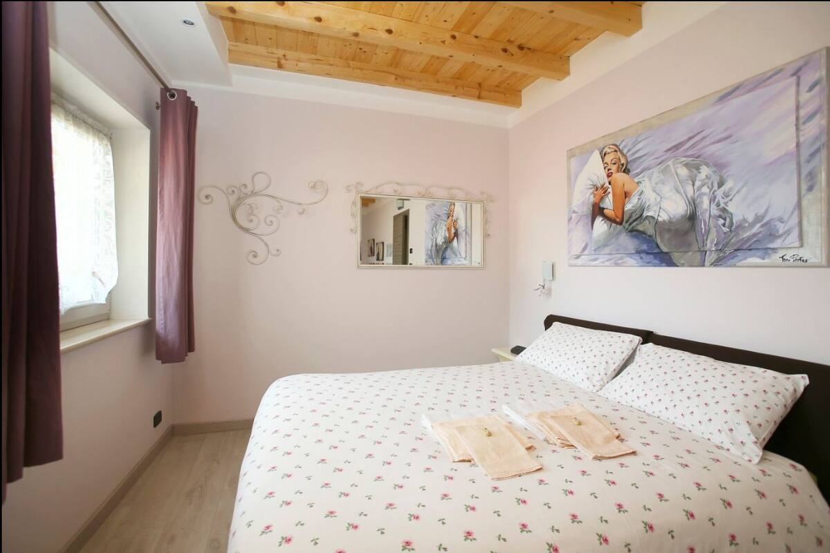 Un dormitorio con cama, un cuadro, un espejo y una ventana con cortinas.
