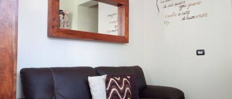 Un canapé en cuir marron agrémenté de deux coussins à motifs, placé devant un mur blanc orné d’un miroir et d’un texte décoratif.