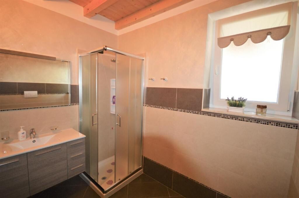 Un bagno con doccia vetrata, lavandino con specchio e finestra con tenda.