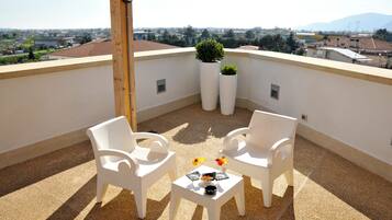 Terraço no telhado com duas cadeiras brancas de plástico, uma mesa pequena com uma tigela e dois copos, e duas plantas em vasos.