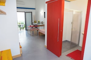 Une pièce comprenant un lit, un bureau, une chaise, une porte rouge et un espace douche.