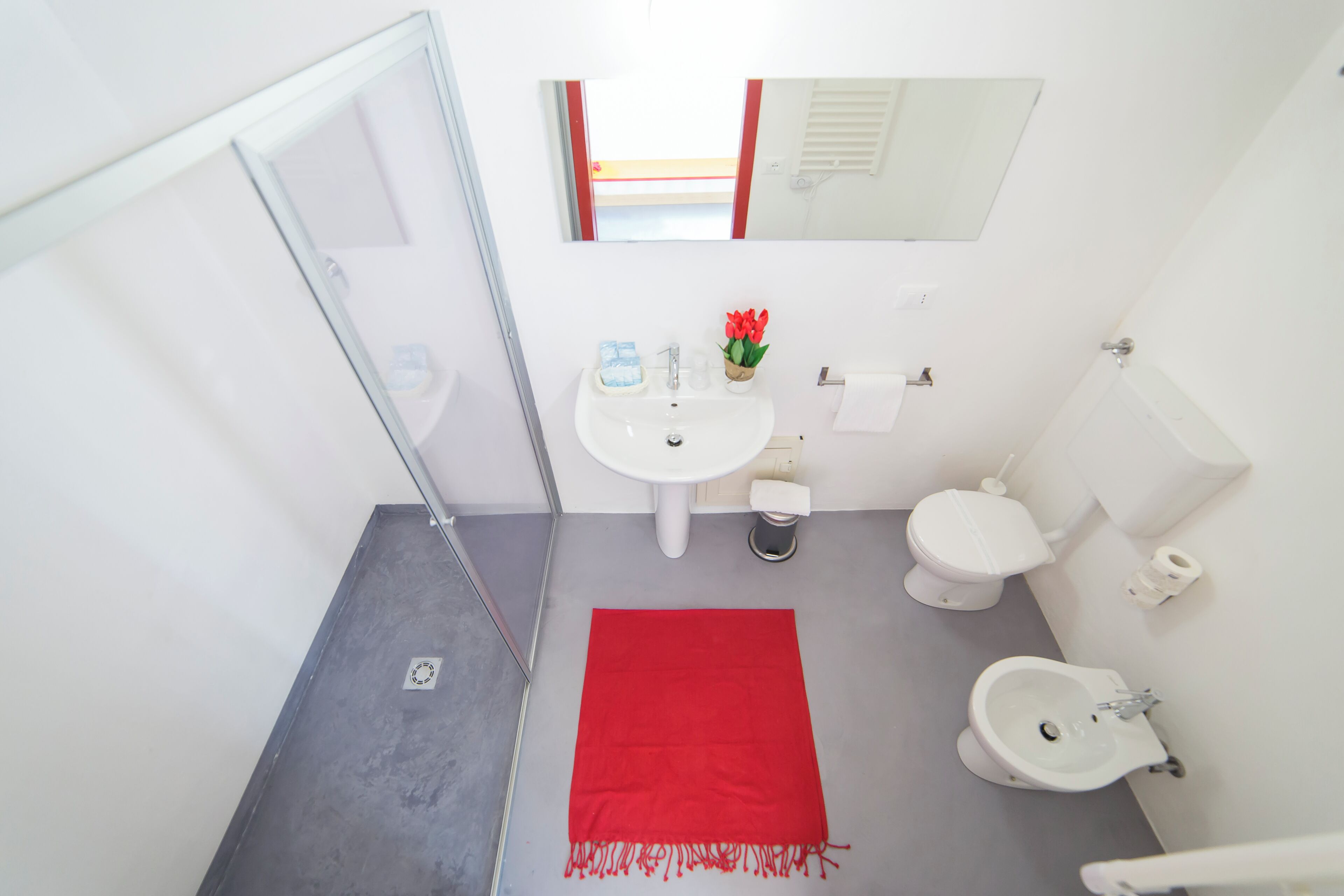 Ein Badezimmer mit einem weißen Waschbecken, Toilette, Bidet und einem roten Teppich.