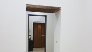 A hallway with a wooden door at the end, a light switch, and a power outlet on the wall. - B&B Napul'è (Naples)