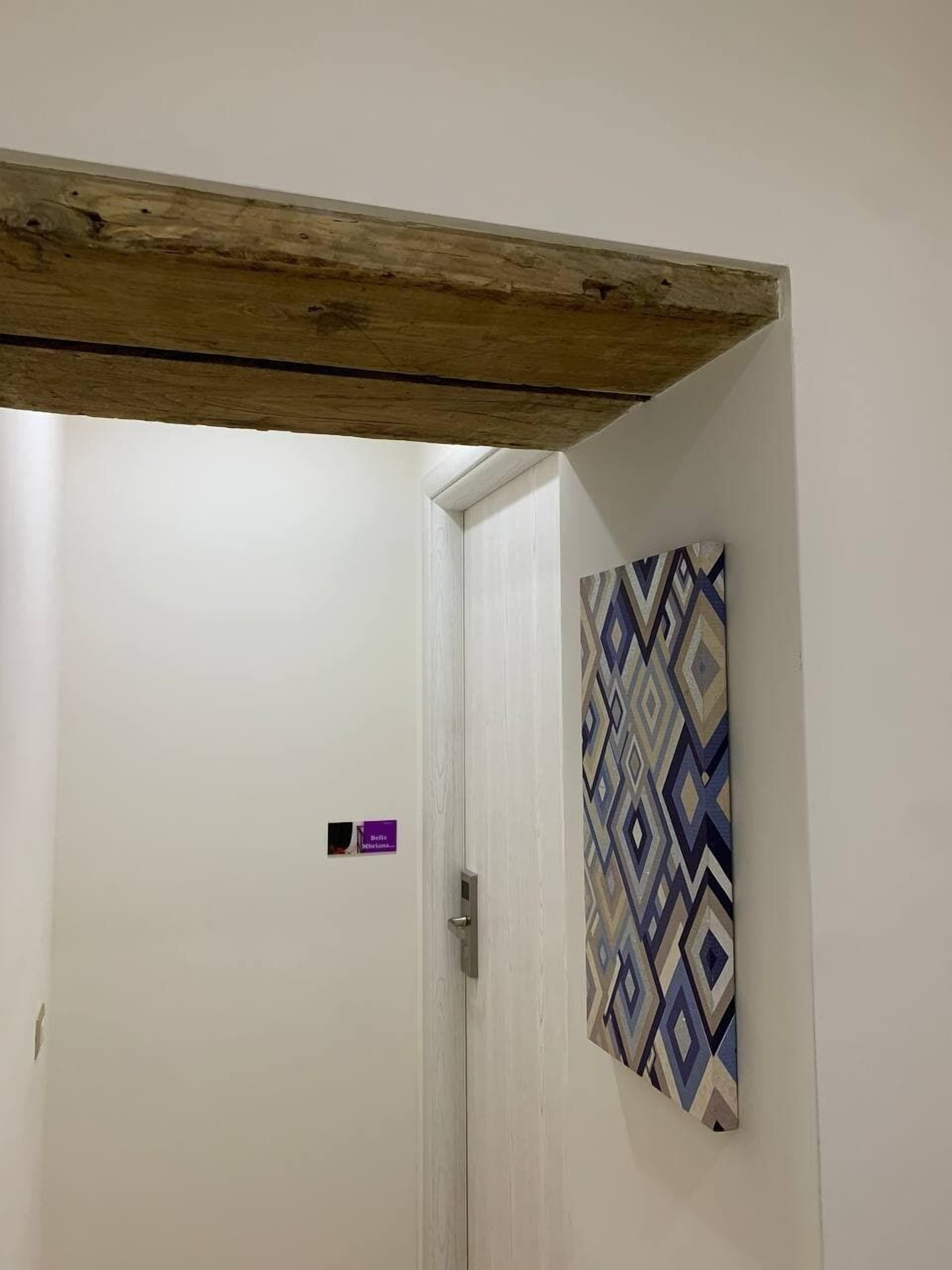 A room with a white door, a wooden ceiling beam, and a patterned wall hanging.