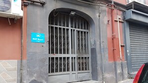 A building with a metal gate, a blue sign with text, and a red car parked nearby. - B&B Napul'è (Naples)