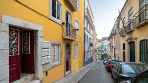 Une ruelle étroite pavée, bordée de bâtiments aux couleurs vives, dont un bâtiment jaune avec une porte rouge et un balcon.