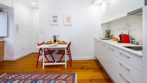 Une cuisine moderne avec des meubles blancs, une table à manger avec des chaises et un îlot de cuisine doté d’un évier et d’un plan de travail.