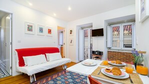 Une chambre moderne avec un canapé rouge, une table de petit-déjeuner avec des croissants et du jus d’orange, et des œuvres d’art accrochées aux murs.
