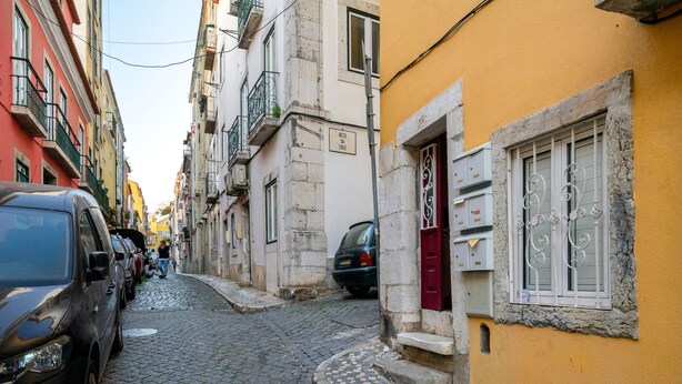 Une ruelle étroite pavée, bordée d’immeubles, avec une voiture garée et une personne qui marche.
