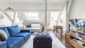 Un salon moderne avec un canapé bleu, un pouf assorti, un téléviseur et un coin repas.