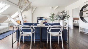 Un salon moderne avec un canapé bleu, des chaises blanches, une table à manger et un téléviseur fixé au mur.