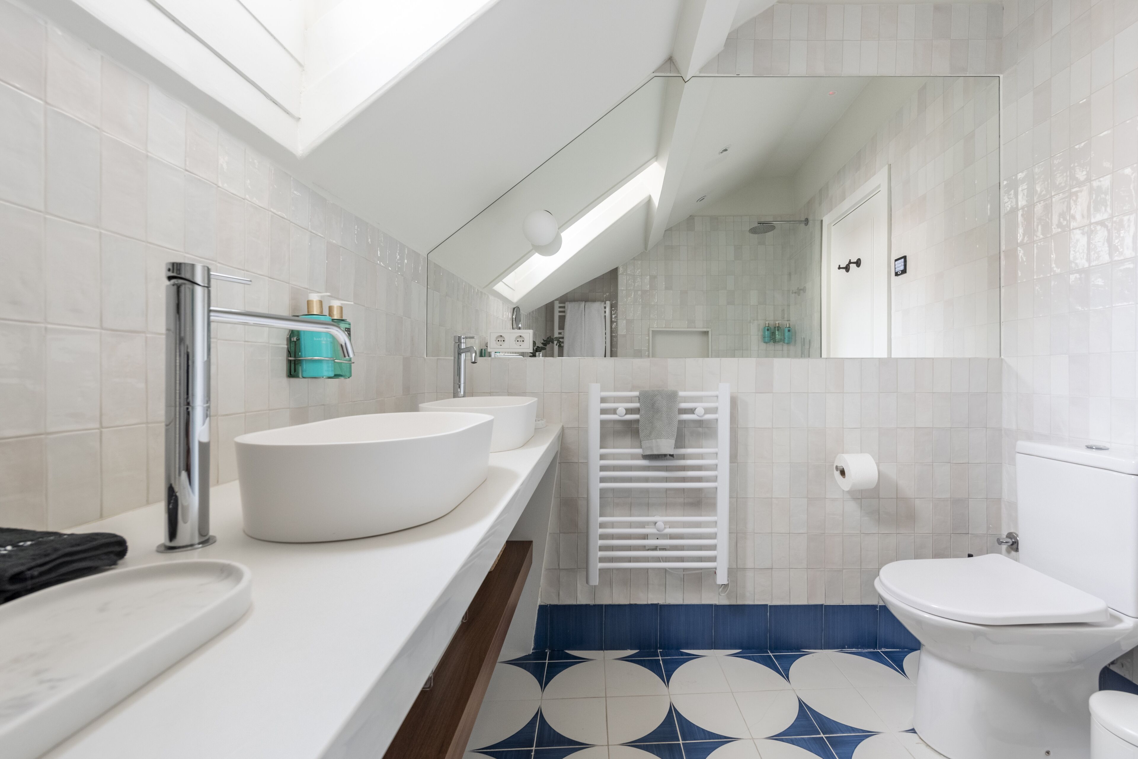 A modern bathroom with a skylight, a large white sink, a toilet, and a blue and white patterned floor.