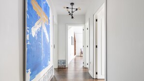 Un couloir orné d’un grand tableau abstrait sur le mur de gauche, une zone carrelée au fond, et un lustre moderne.