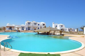 Una piscina al aire libre, sombrillas, sillones reclinables de piscina