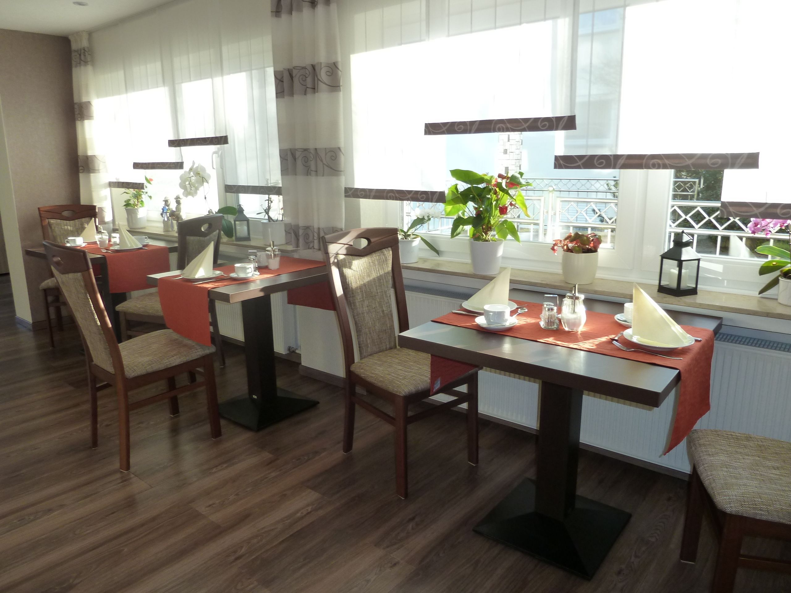 Un comedor con mesas y sillas de madera, plantas en macetas y vistas a la ciudad a través de amplios ventanales.