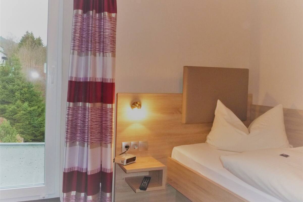 A hotel room with a bed, a nightstand with a lamp, and a window with curtains.