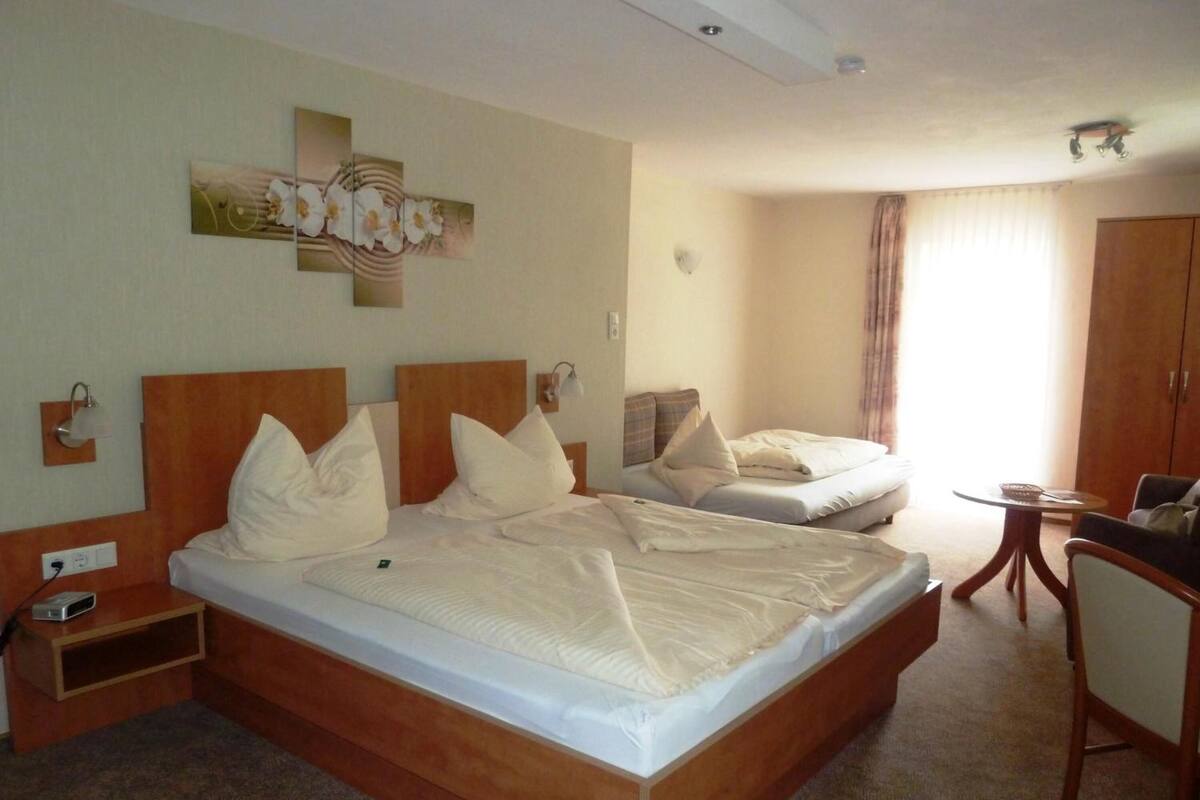 A hotel room with a large bed, a bedside table, a lamp, a small table, and a wardrobe.
