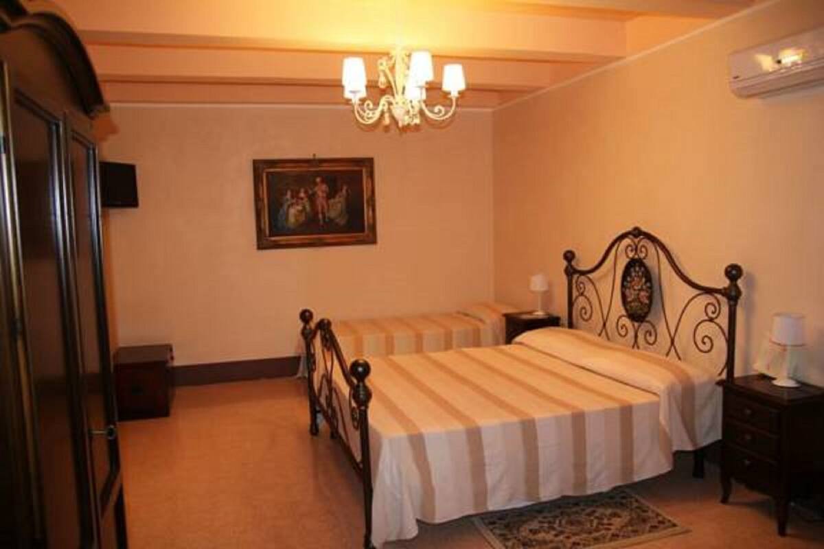 A bedroom with two single beds, a chandelier, a painting on the wall, and a small bedside table with a lamp.