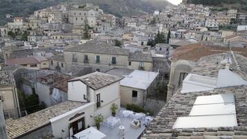 Un pueblo en una ladera densamente poblado con arquitectura tradicional, tejados de teja y una terraza en la azotea con mesas y sillas.