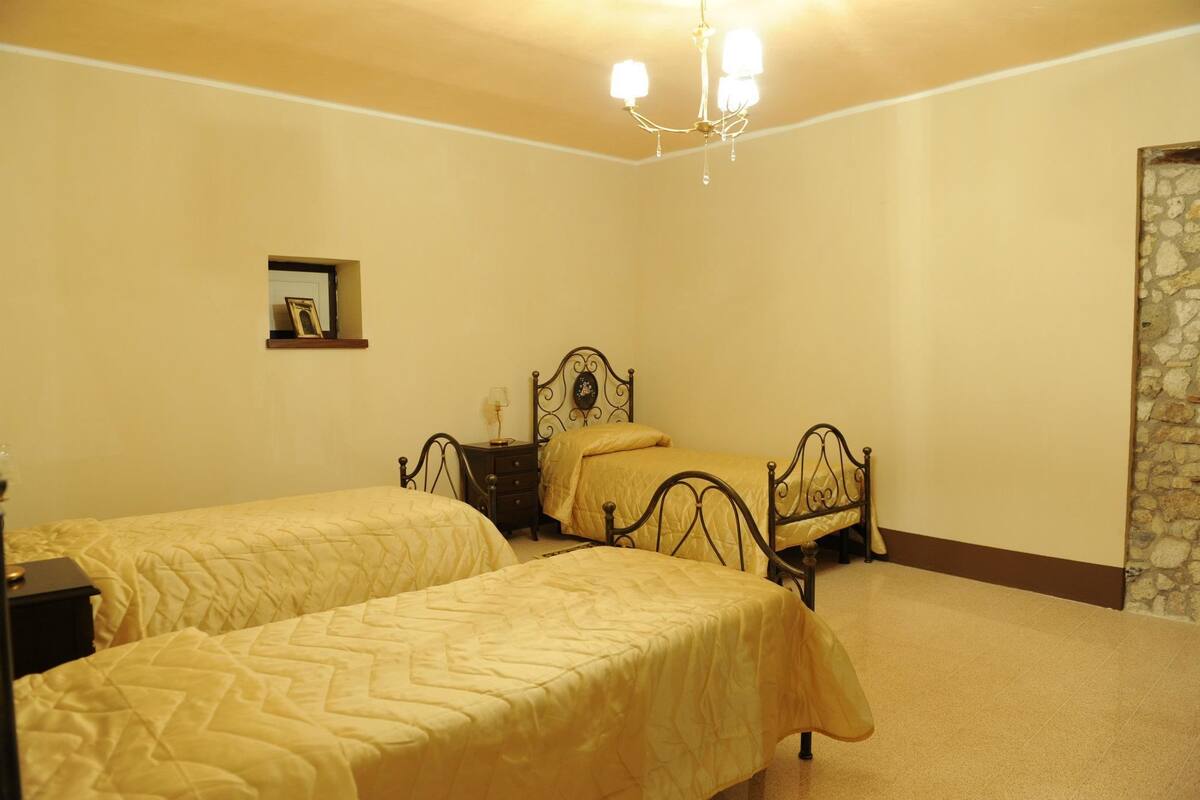 A bedroom with two single beds, a nightstand, a dresser, a chandelier, and a stone wall.