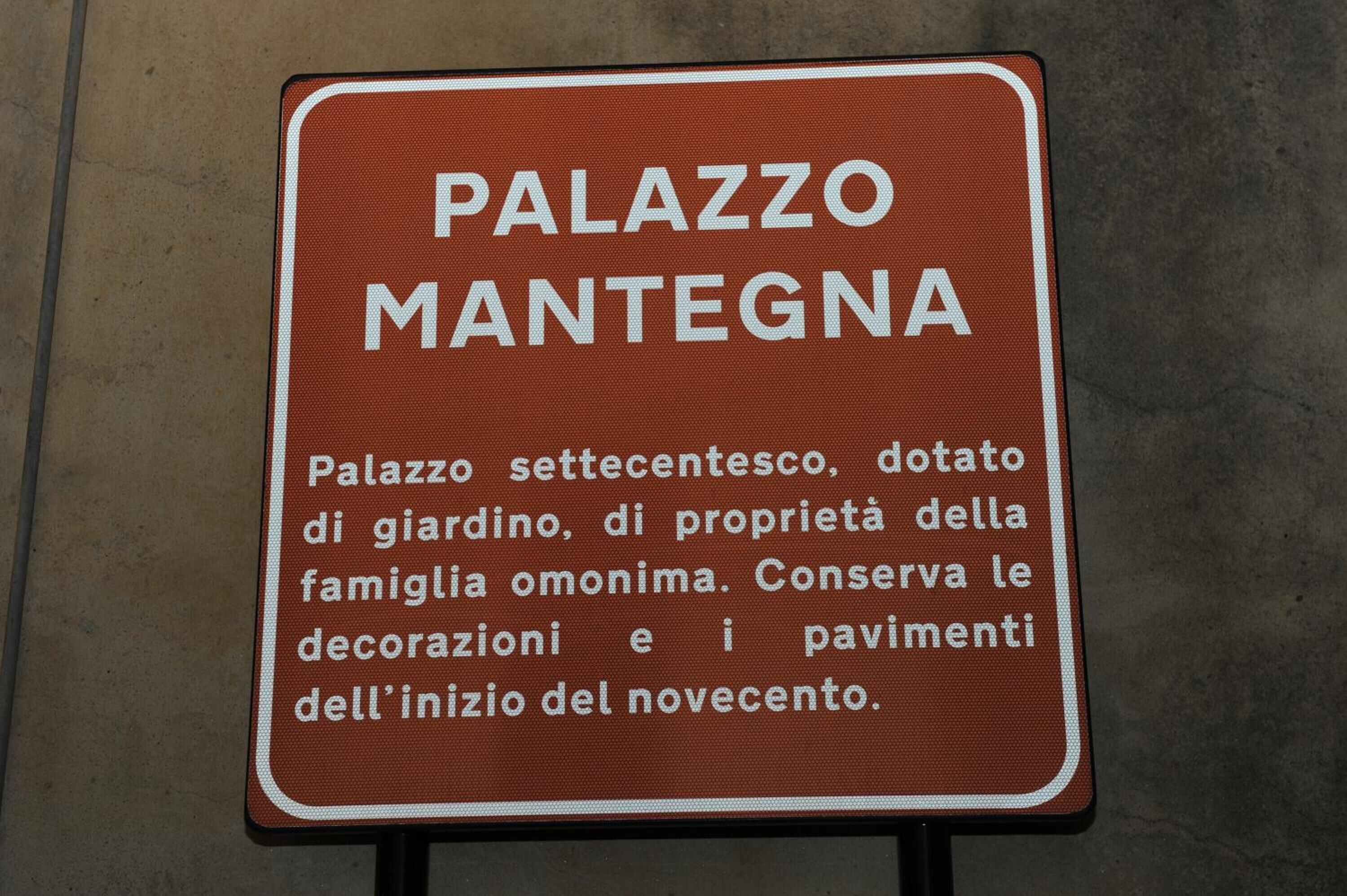 A sign for Palazzo Mantegna, a historic building with a courtyard, owned by the Omoni family, featuring preserved decorations and pavements from the 15th century.