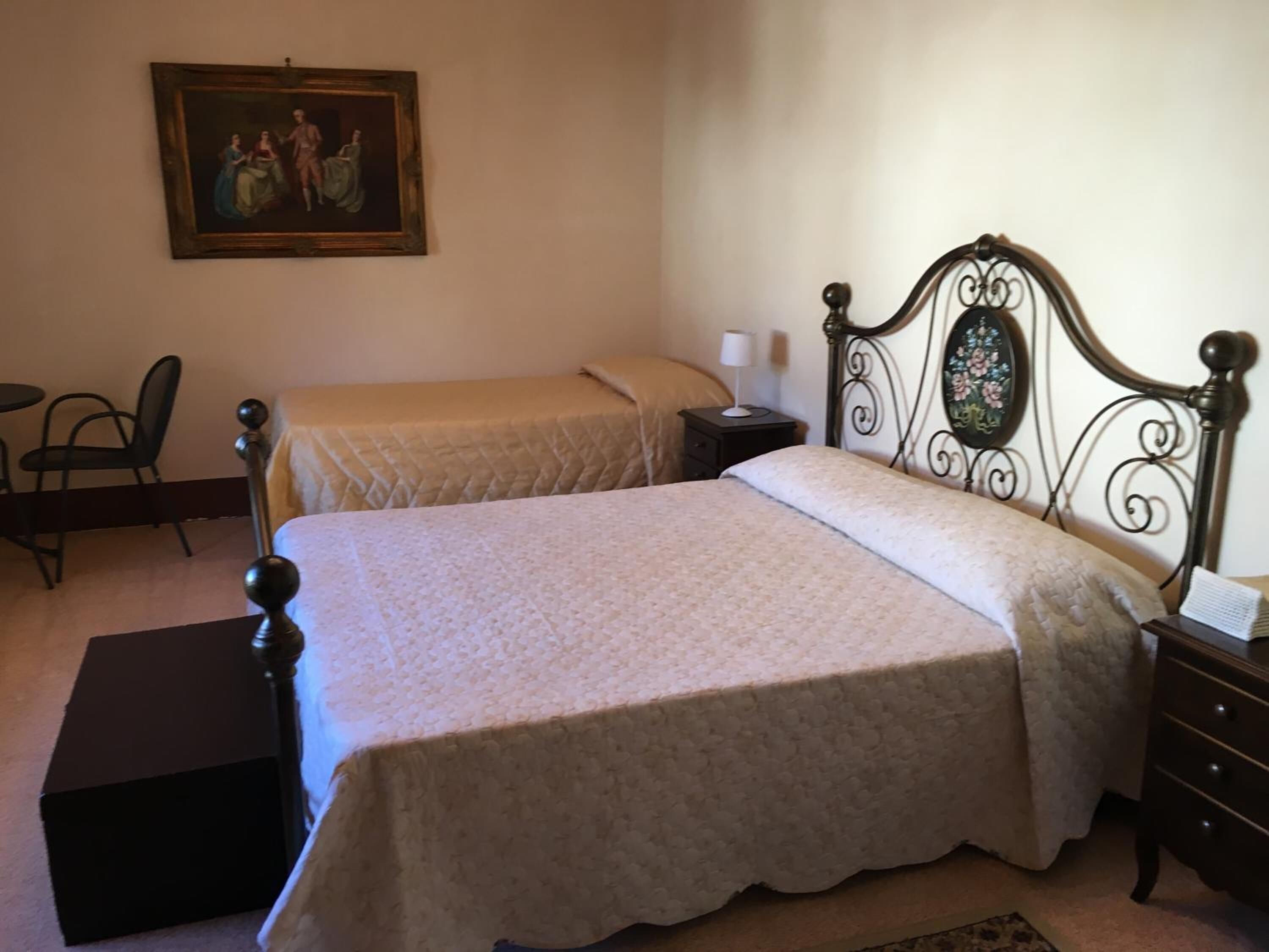 A bedroom with two single beds, a nightstand with a lamp, a chair, and a painting on the wall.